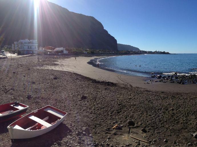 Vistas a la playa donde se ve la montaña, algunas casas y unos barcos en la orilla