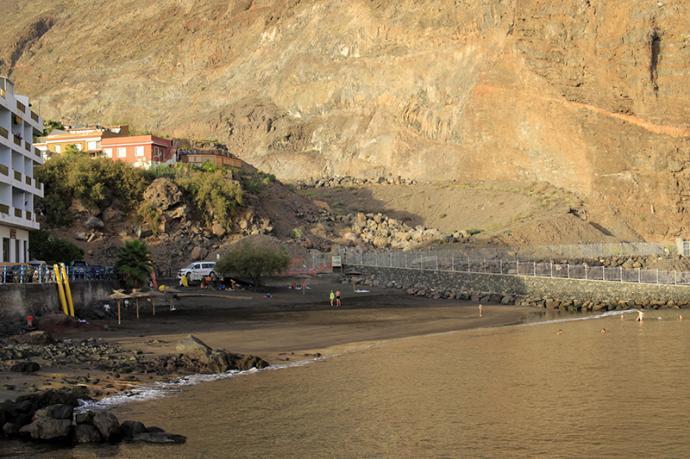 Playa al lado de edificios y con un paseo de piedras pegado a la montaña