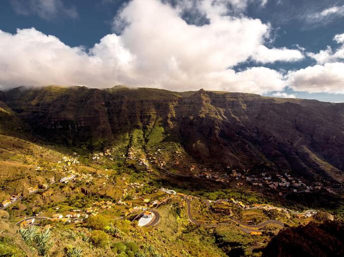 Vistas de las montañas en la Gomera, llenas de vegetación. Se ven casas y vistas del cielo.