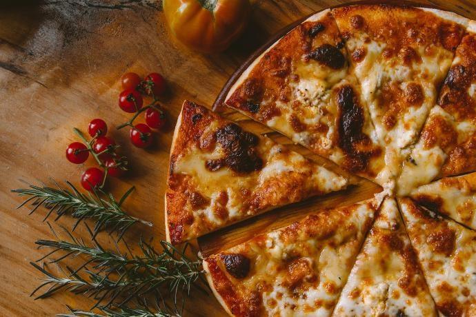 Pizza de masa fina hecha al horno, junto a unos pequeños tomates y otros ingredientes sobre una mesa marrón